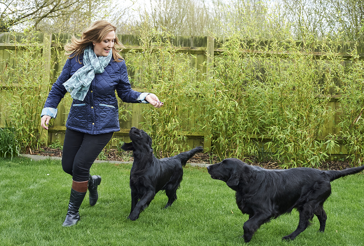 Jenny Campbell playing with two Flat Coated Retrievers in a garden